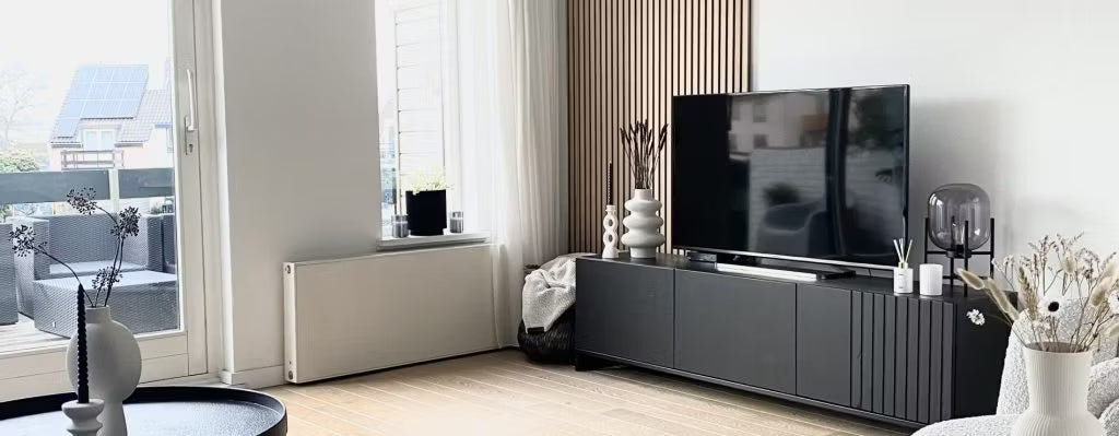 Moderne stue med sort tv-bord, fladskærms-tv, dekorative vaser og store vinduer med naturligt lys med udsigt til terrassen; Akupanel på den ene væg.
